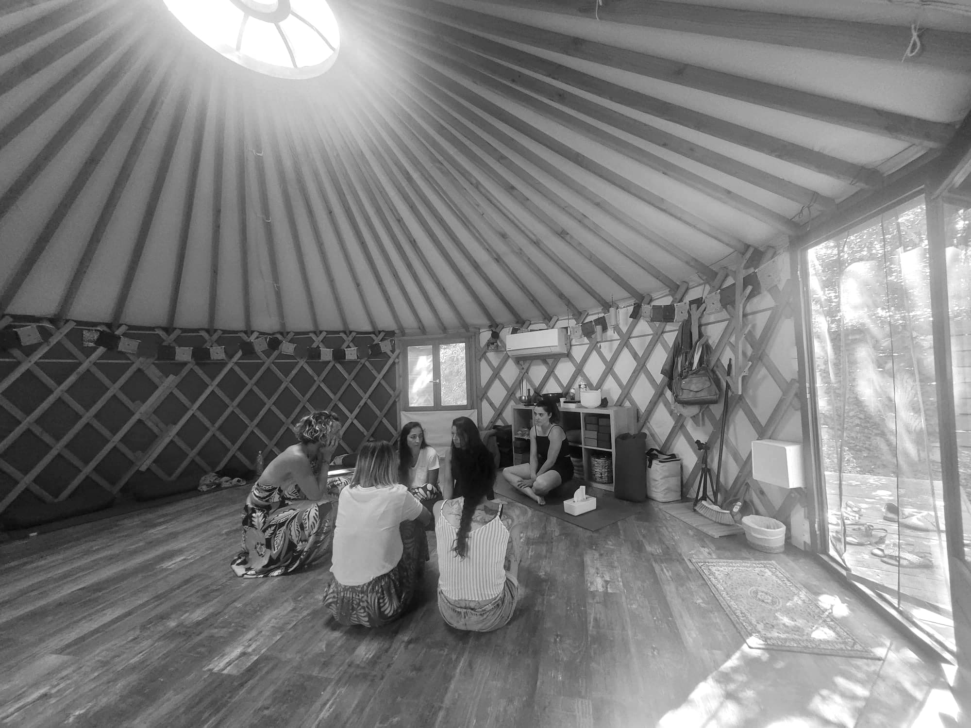 Une journée de constellations sous une yourte : des participantes assises en cercle, dans la lumière du puits et de la baie vitrée.